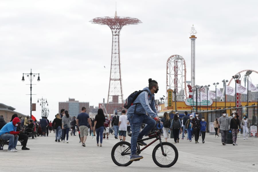 A young man wearing a protective face mask rides his bicycle along a fairly crowded Coney Island boardwalk during the current coronavirus outbreak, the afternoon of Sunday, May 24, 2020, in New York. No swimming was allowed and social distancing reminders were abundant on the beach as Memorial Day weekend kicked off the first weekend of summer.