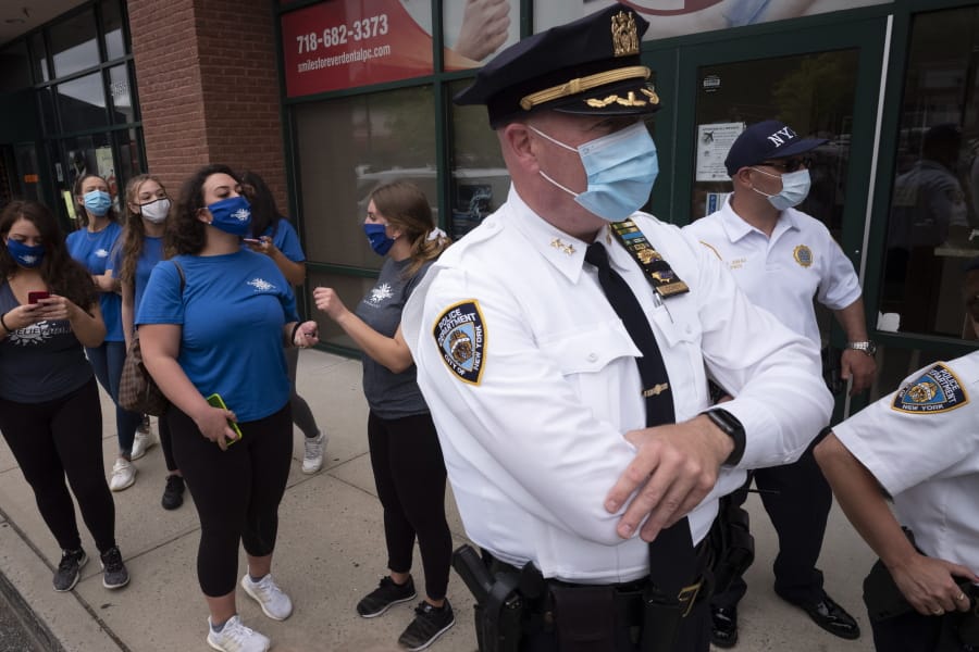 Tanning salon workers, left, stand behind police outside the Staten Island business, Thursday, May 28, 2020, in New York. Owner Bobby Catone opened the salon briefly Thursday morning in defiance of a law requiring non-essential businesses to remain closed during the coronavirus pandemic.