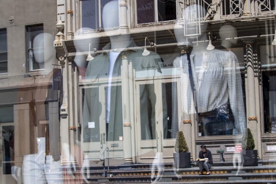A woman sitting on a stoop reading a book in the sun is seen reflected by a closed clothing store&#039;s window on West Broadway, Thursday, May 7, 2020, in the SoHo neighborhood of the Manhattan borough in New York. The U.S. government is poised to report the worst set of job numbers since record-keeping began in 1948, a stunning snapshot of the toll the coronavirus has taken on a now-shattered economy.