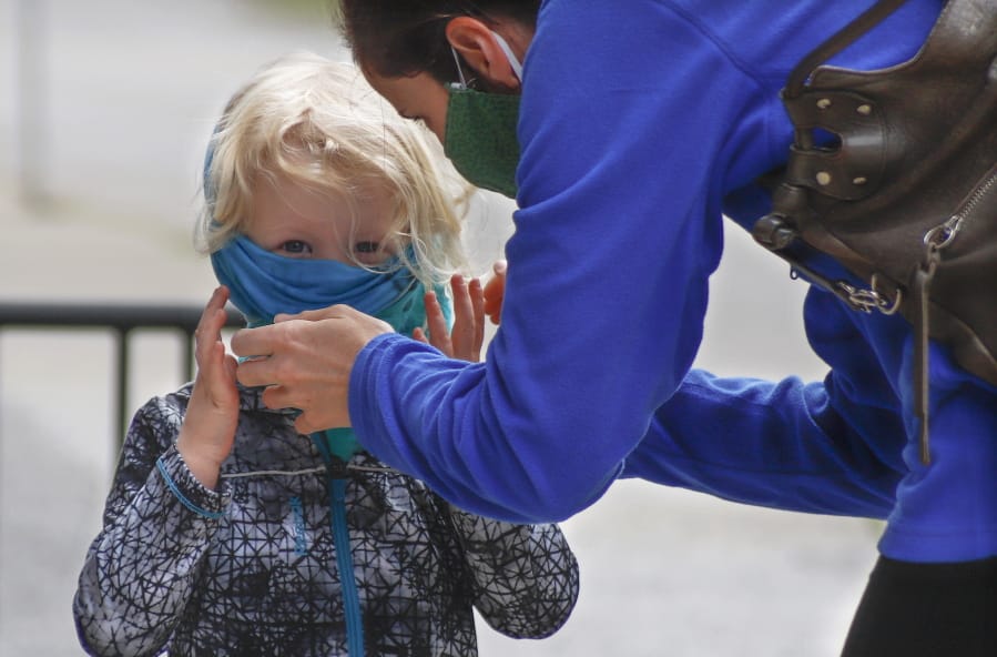 Bridget Kreider, right, helps her three-year-old daughter Maggie pull on her protective face covering before entering a store, Wednesday, May 20, 2020, in Harmony, Pa. Customers entering stores are required to wear face coverings to help prevent the spread of the new coronavirus during the COVID-19 pandemic under the state yellow phase reopening guide.