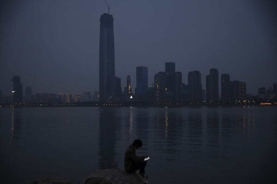 FILE - In this April 5, 2020, file photo, a man checks his mobile phone along the Yangtze River in Wuhan in central China&#039;s Hubei province. As governments around the world consider how to monitor new coronavirus outbreaks while reopening their societies, many are starting to bet on smartphone apps to help stanch the pandemic.