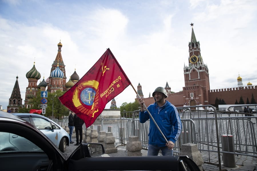 A man poses for a photo with a red flag in front of the closed Red Square during the 75th anniversary of the Nazi defeat in World War II in Moscow, Russia, Saturday, May 9, 2020. Victory Day is Russia&#039;s most important secular holiday and this year&#039;s observance had been expected to be especially large because it is the 75th anniversary, but the Red Square military parade and a mass procession called The Immortal Regiment were postponed as part of measures to stifle the spread of coronavirus.