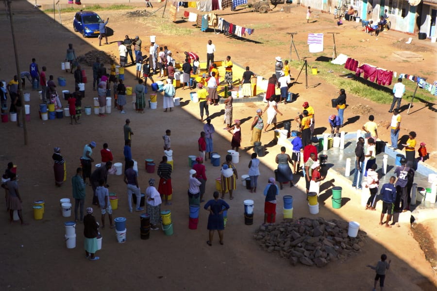 In this April, 24, 2020, photo, people wait to fetch water from a row of communal taps that the group Doctors Without Borders provided in a suburb of Harare, Zimbabwe. For people around the world who are affected by war and poverty, the simple act of washing hands is a luxury. In Zimbabwe, clean water is often saved for daily tasks like doing dishes and flushing toilets.