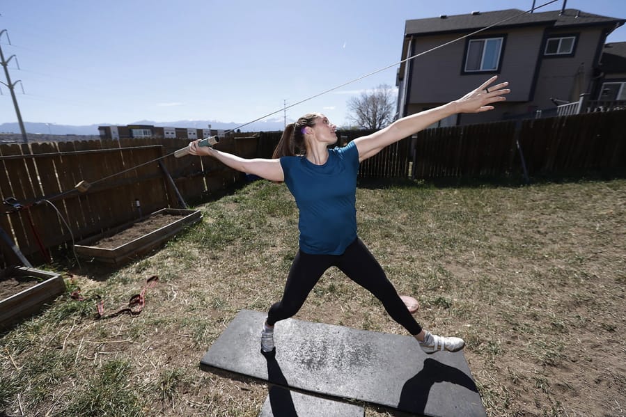 Kara Winger uses a cable system to simulate throwing a javelin as she trains outside her home in Colorado Springs, Colo., Wednesday, April 29, 2020. The renovated home of three-time Olympic javelin thrower Kara Winger now has all the training amenities she needs, including cable. No premium channels on this cable. It&#039;s just a basic wire she and her husband installed in the backyard to help her work on her technique. She throws a metal pipe along the angled cable to simulate javelin tosses.