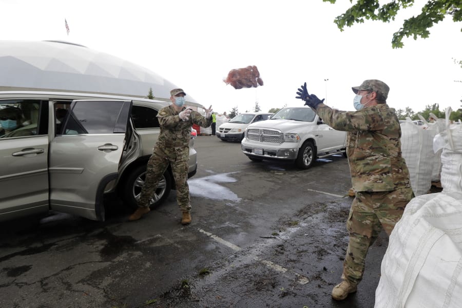 Members of the Washington National Guard toss a bag of potatoes as they load a waiting car, Thursday, May 14, 2020, during the free distribution of 200,000 pounds of potatoes provided by the Washington State Potato Commission in Tacoma, Wash. Most of the potatoes were donated by farmers across the state who have not been able to sell to their regular restaurant customers due to the coronavirus pandemic. (AP Photo/Ted S.