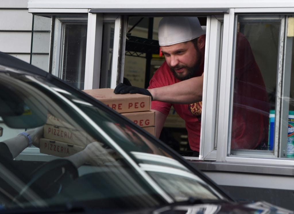 In this March 2020 file photo, Dante Cistulli, owner of Square Peg Pizzeria in Glastonbury, hands pizzas to a customer through his restaurant's drive-thru window.
