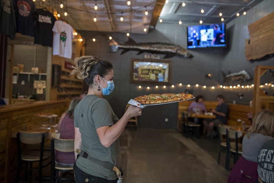Crystal Badley of Backwoods Brewing Company wears a protective mask as she serves a fresh pizza to customers in Carson on Thursday afternoon. Carson, which is located in Skamania County, is already in Phase 2 of the reopening plan outline by Gov. Jay Inslee during the COVID-19 pandemic.