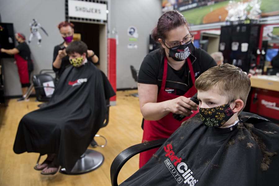 Manager Melissa New, second from right, lends a hand as Elliot Reichstein, 7, of Ridgefield gets a much-needed trim at SportClips on Monday afternoon in Hazel Dell after being in quarantine for COVID-19.