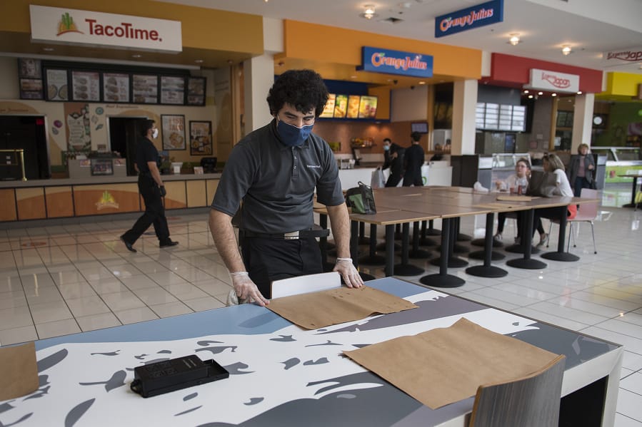 Michael Figuero of Vancouver, who works in housekeeping at Vancouver Mall, keeps tables clean in the food court while encouraging social distancing on Wednesday afternoon. The mall reopened for in-person shopping on Wednesday, although restrictions are still in place, including fewer seats at the food court tables.