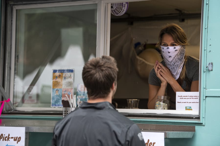 Funky Fresh Juice co-owner Rebekah Trigg, right, helps customers at the Vancouver Farmers Market in downtown Vancouver. As Clark County applies to enter Phase 3 of reopening, masks are required across the state.