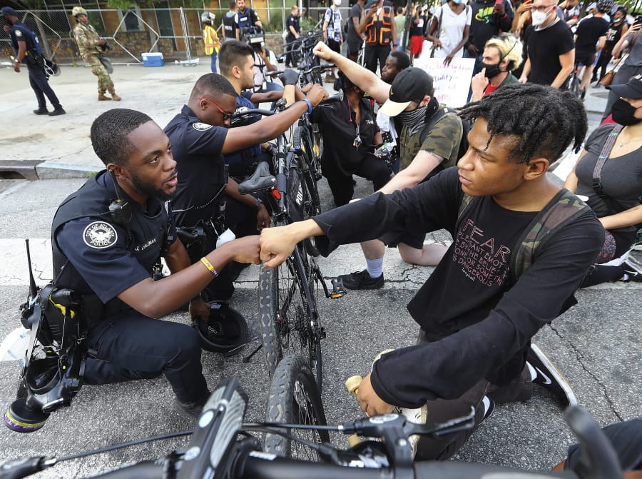 FILE - In this June 3, 2020, file photo, Atlanta Police Officer J. Coleman, left, and protester Elijah Raffington, of Sandy Springs, fist bump in a symbolic gesture of solidarity outside the CNN Center at Olympic Park, in Atlanta. George Floyd, a black man, died after being restrained by Minneapolis police officers on May 25 and his death sparked protests. Black officers find themselves torn between two worlds when it comes to the protests against police brutality happening around the U.S.