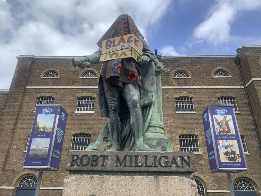The statue of Robert Milligan, a noted West Indian merchant, slaveholder and founder of London&#039;s global trade hub, West India Docks, stands covered in a sack-cloth and sign reading Black Lives Matter, outside the Museum of London Docklands, Tuesday June 9, 2020.  The recent death of George Floyd who died after a U.S.  officer pressed his knee into his neck, has prompted investigations into the lorded promotion of many historical figures who gave money to philanthropic enterprises, gaving their names to British city areas, statues and landmarks, but gained much of their wealth from the slave trade.
