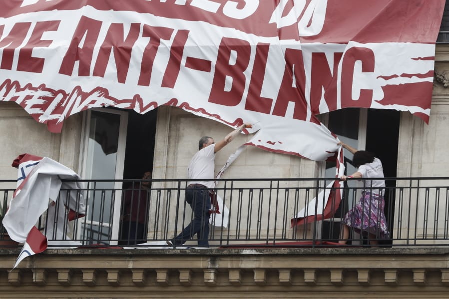 Residents of a building cut up a banner which was lowered from the roof of his building by far-right protestors with the Identitarian nationalist French movement during a march against police brutality and racism in Paris, France, Saturday, June 13, 2020, organized by supporters of Adama Traore, who died in police custody in 2016 in circumstances that remain unclear despite four years of back-and-forth autopsies. The march is expected to be the biggest of several demonstrations Saturday inspired by the Black Lives Matter movement in the U.S., and French police ordered the closure of freshly reopened restaurants and shops along the route fearing possible violence.