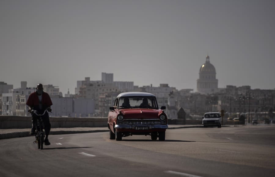 An American classic car and bicycle share the road Thursday in Havana, Cuba, as a dust cloud blankets the city.