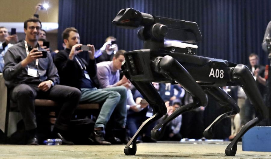 A Boston Dynamics SpotMini robot walks through a conference room during a robotics summit in Boston.