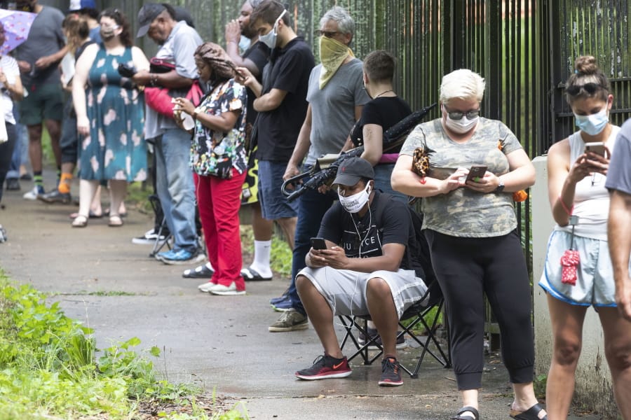 FILE - In this June 9, 2020, file photo, Steven Posey checks his phone as he waits in line to vote at Central Park in Atlanta. Voters reported wait times of three hours. When some Georgia voters endured a pandemic, pouring rain and massive waits earlier this month to cast their ballot, President Donald Trump and other Republicans blamed local Democrats for presiding over chaos.