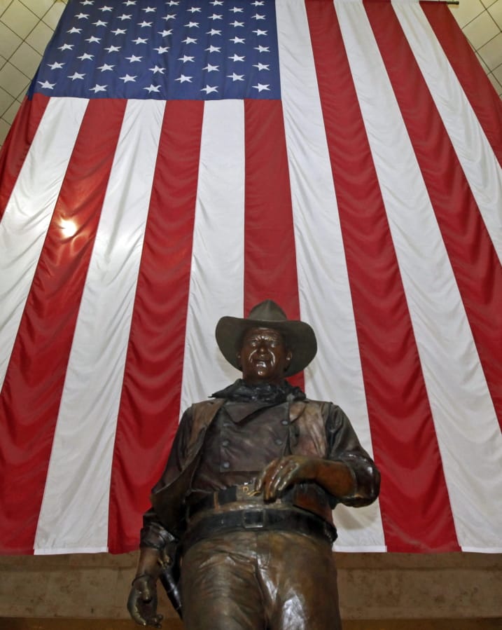 FILE - In this Sept. 11, 2011, file photo, a bronze statue of late actor John Wayne stands before a four-story high United States flag at John Wayne Orange County Airport in Santa Ana, Calif. In the latest move to change place names in light of U.S. racial history, leaders of Orange County&#039;s Democratic Party are pushing to drop film legend Wayne&#039;s name, statue and other likenesses from the county&#039;s airport because of his racist and bigoted comments.