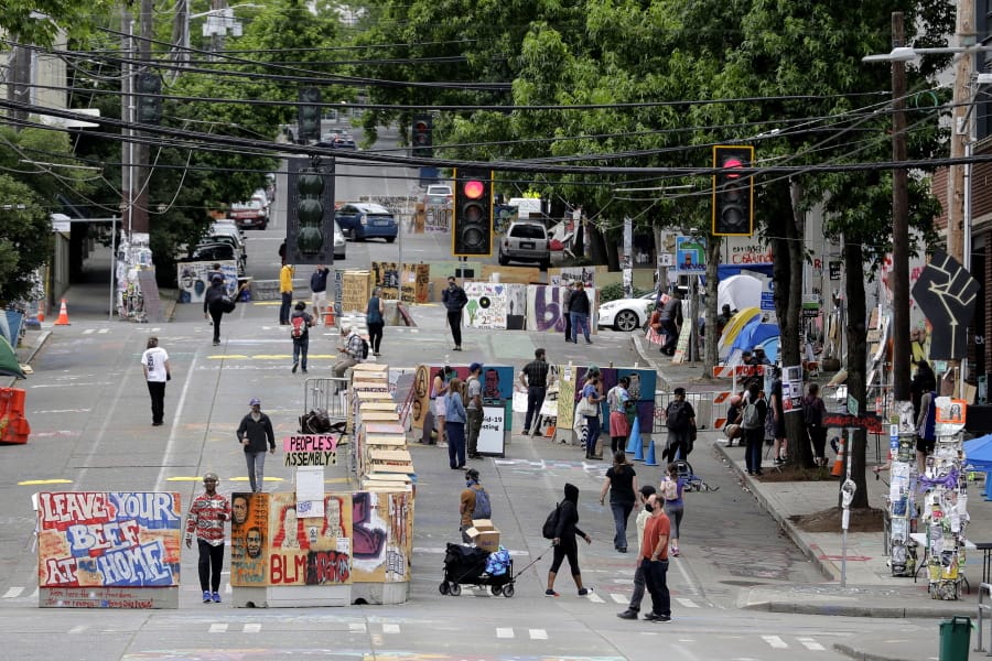 Visitors walk by the barricades, Wednesday, June 24, 2020, near the Seattle Police East Precinct building inside the CHOP (Capitol Hill Occupied Protest) zone in Seattle. The area has been occupied since a police station was largely abandoned after clashes with protesters, but Seattle Mayor Jenny Durkan said Monday that the city would move to wind down the protest zone following several nearby shootings and other incidents that have distracted from changes sought peaceful protesters opposing racial inequity and police brutality. (AP Photo/Ted S.