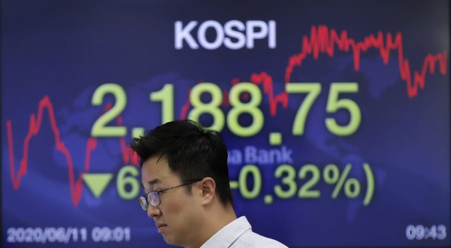 A currency trader walks by a screen showing the Korea Composite Stock Price Index (KOSPI) at the foreign exchange dealing room in Seoul, South Korea, Thursday, June 11, 2020. Asian shares were mostly lower Thursday, with Tokyo dropping more than 1% as the Japanese yen gained after the Federal Reserve said it would keep interest rates low through 2022.