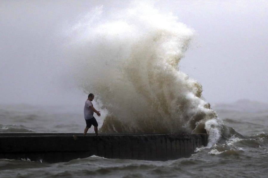 A wave crashes as a man stands on a jetty near Orleans Harbor in Lake Pontchartrain in New Orleans, Sunday, June 7, 2020, as Tropical Storm Cristobal approaches the Louisiana Coast.