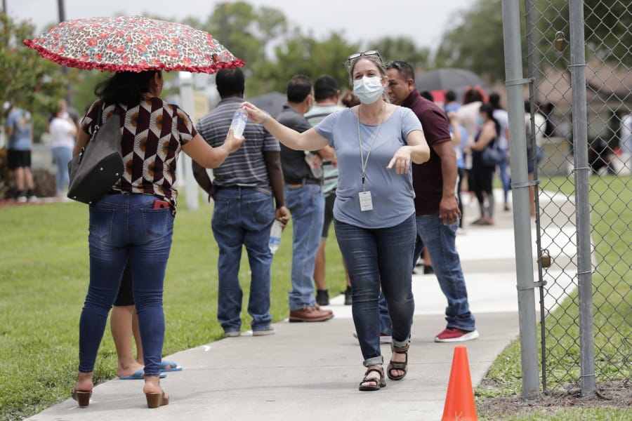 In this Sunday, June 7, 2020, photo, Gretel Cacerces, right, passes out bottled water to those standing in line for COVID-19 testing at the Florida Department of Health in Collier County amid the new coronavirus pandemic in Immokalee, Fla. Even as the pace of new cases has moderated in the state of Florida, this poor farmworking town in rural Florida is in the throes of an outbreak.