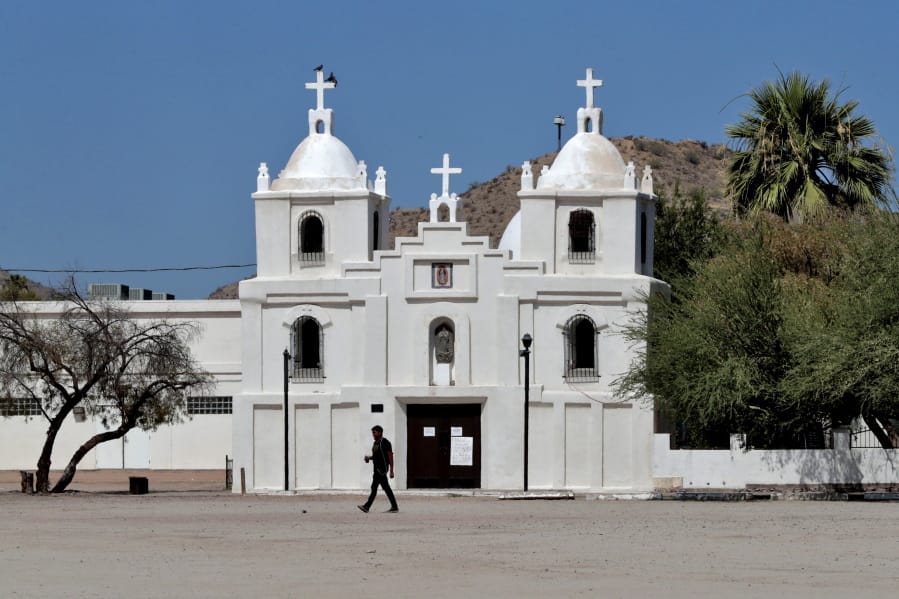 In this June 13, 2020, photo, a man walks past Our Lady of Guadalupe church in Guadalupe, Ariz. As the coronavirus spreads deeper across America, it&#039;s ravaging through the homes and communities of Latinos from the suburbs of the nation&#039;s capital to the farm fields of Florida to the sprawling suburbs of Phoenix and countless communities in between.