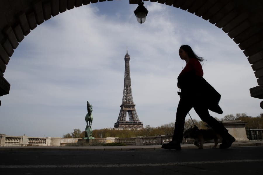 A woman walks her dog on a Paris bridge April 7, with the Eiffel Tower in background, during a nationwide confinement to counter the COVID-19.