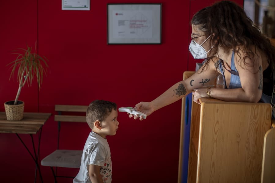 Hugo, 3, has his temperature taken by a teacher as he arrives at Cobi kindergarten in Barcelona, Spain, Friday, June 26, 2020. Spain&#039;s cabinet will extend the furlough schemes adopted during the coronavirus lockdown that brought the economy to a standstill until the end of September.