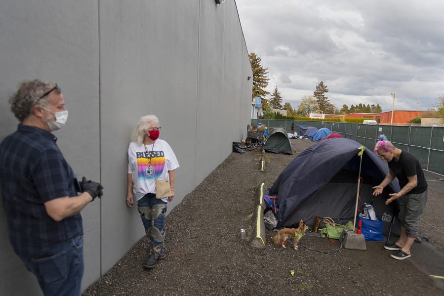 Patrick Quinlan, from left, and Linda Karschney of Living Hope Church chat with Mandi Holper as she settles in for the evening with her dog, Baby, at a temporary homeless encampment outside the church on May 5.