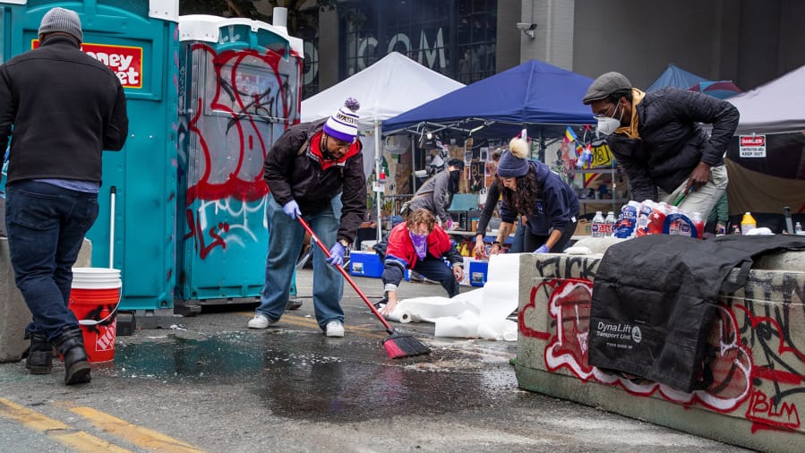 Protesters clean blood off 12th Avenue in front of the East Seattle Police Precinct on Monday morning after an early morning shooting left one person dead and another injured between East Pike Street and East Pine Street in Seattle on June 29, 2020.