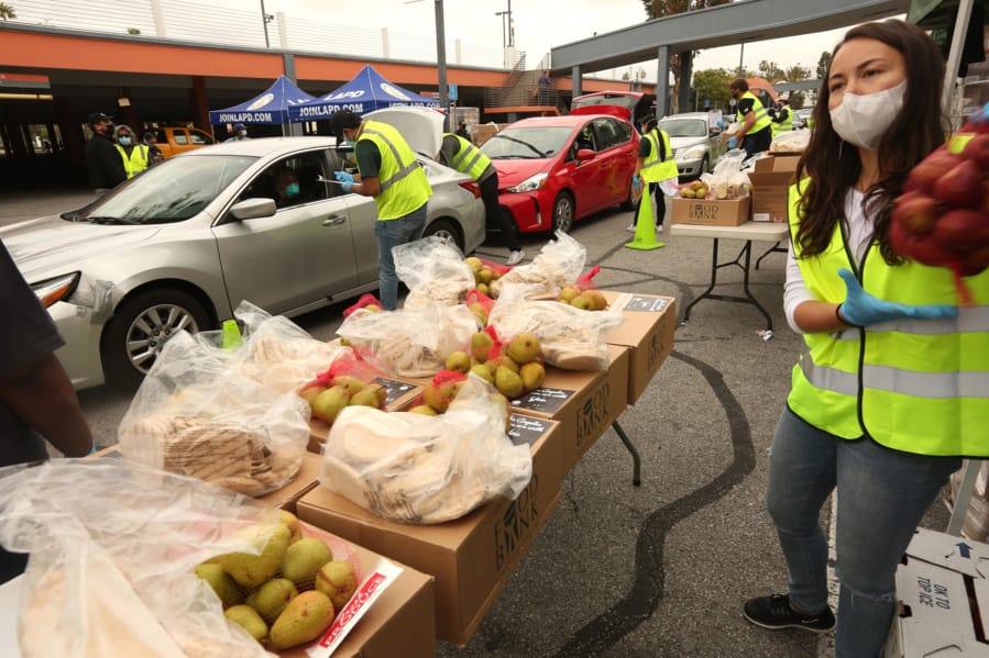 Volunteer Emi Lea Kamemoto, right, moves bags of food to a nearby table as other volunteers load up people&#039;s cars with boxes of food in the Crenshaw District on April 17, 2020. Cars lined up for blocks for the Los Angeles County Federation of Labor, in collaboration with Labor Community Services, the Los Angeles Regional Food Bank, and Councilmember Marqueece Harris-Dawson (CD-8), to distribute food for more than 2,500 families, or 10,000 individuals, affected by the COVID-19 crisis at the Baldwin Hills Crenshaw shopping center parking lot.