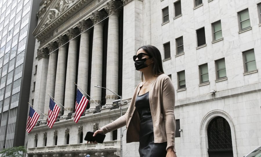 A woman wearing a mask passes the New York Stock Exchange, Tuesday, June 30, 2020, during the coronavirus pandemic.