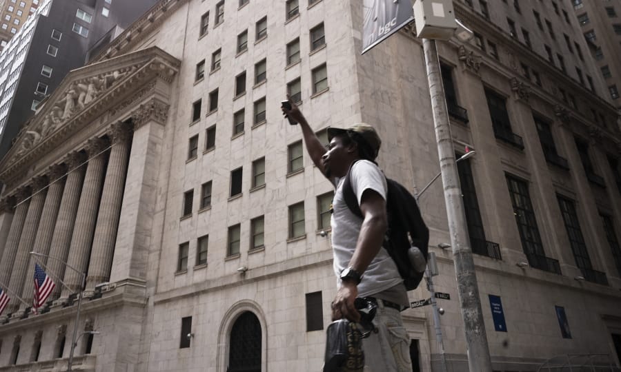 A man lifts his arm as he walks by the New York Stock Exchange, Thursday, July 30, 2020. Stocks are falling on Wall Street Thursday after reports showed that layoffs are continuing at a stubborn pace and that the U.S. economy contracted at a nearly 33% annual rate in the spring.