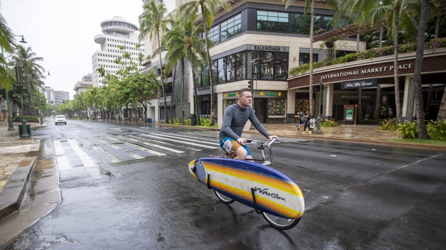 An Oahu resident packing his surfboard on his bike rides through a deserted Waikiki on Kalakaua Ave., Sunday, July 26, 2020, in Honolulu. Most of Oahu residents are taking shelter preparing for the arrival of Hurricane Douglas.