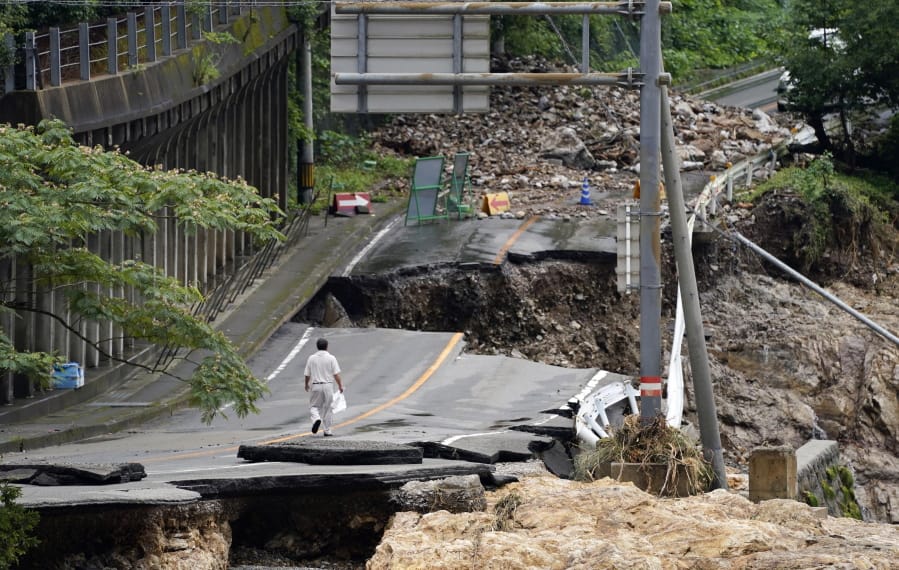 A man walks on heavily damaged road following a heavy rain in Kumamura, Kumamoto prefecture, southern Japan Monday, July 6, 2020. Rescue operations continued and rain threatened wider areas of the main island of Kyushu.