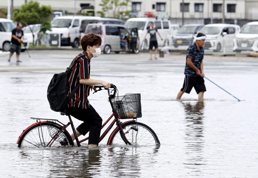 A man on a bicycle makes his way through a flooded road following heavy rains in Kurume, Fukuoka prefecture, southern Japan Wednesday, July 8, 2020. Floodwaters flowed down streets in southern Japanese towns hit by heavy rains.