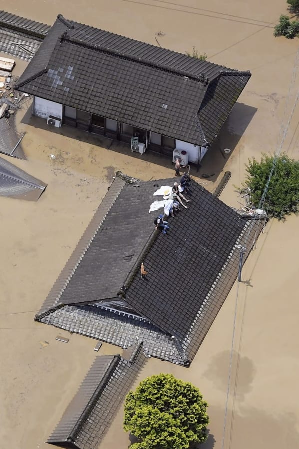 Residents are stranded on the rooftop of a house submerged in muddy waters that gushed out from the Kuma River in Hitoyoshi, Kumamoto prefecture, southwestern Japan, Saturday, July 4, 2020. Heavy rain triggered flooding and mudslides on Saturday, leaving more than a dozen missing. More than 75,000 residents in the prefectures of Kumamoto and Kagoshima were asked to evacuate following pounding rains overnight.