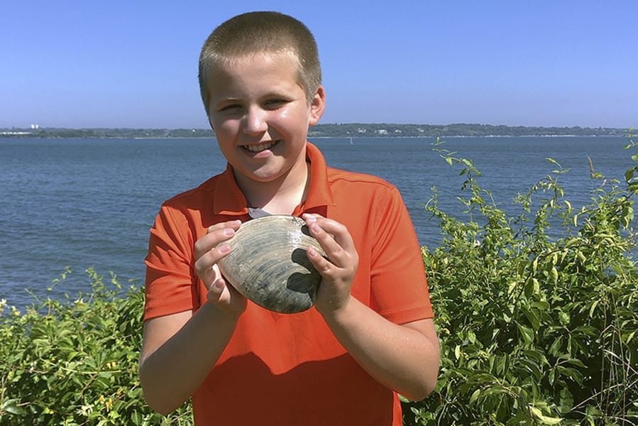 In this Tuesday, July, 28, 2020, photo provided by the University of Rhode Island, Cooper Monaco holds the large quahog he found Monday while clamming with his grandfather in Westerly, R.I. The quahog is more than five inches across and weighing more than two pounds, and is among the largest ever harvested in the state. The mollusk was donated to the University of Rhode Island&#039;s Marine Science Research Facility.