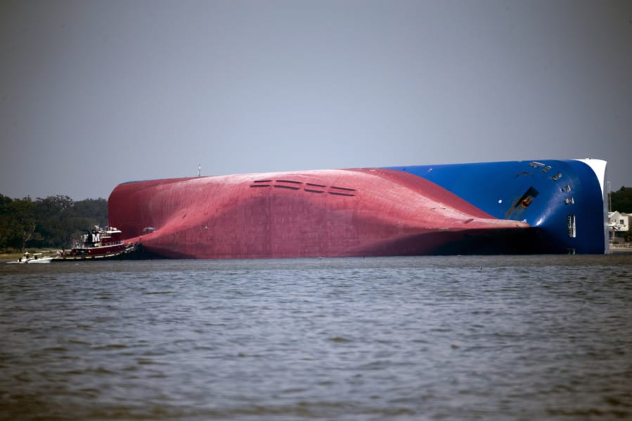 FILE - In this Sept. 9, 2019, file photo, a Moran tugboat nears the stern of the capsizing vessel Golden Ray near St. Simons Sound off the coast of Georgia. The salvage team salvage team is seeking a federal permit to surround the shipwreck with a giant mesh barrier to contain any debris when they cut the ship apart. (AP Photo/Stephen B.