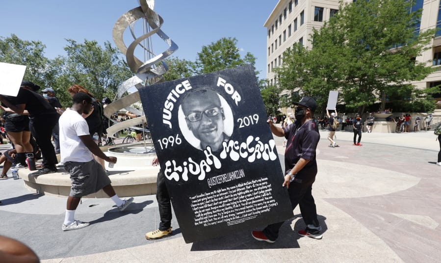 FILE - In this June 27, 2020, file photo, demonstrators carry a giant placard during a rally and march over the death of 23-year-old Elijah McClain outside the police department in Aurora, Colo. Multiple suburban Denver police officers have been placed on paid administrative leave amid an investigation into photos of them related to the case of a Black man who died last summer after he was stopped and restrained, police said Monday, June 29, 2020. The interim police chief of the city of Aurora, Vanessa Wilson, said in a statement that the suspended officers were &quot;depicted in photographs near the site where Elijah McClain died.&quot; But her statement did not provide more details about what the images show.
