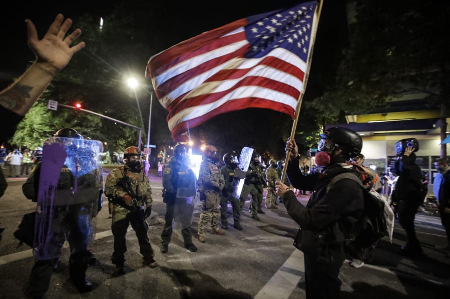 A demonstrator waves a U.S. flag in front of federal officers after tear gas is deployed during a Black Lives Matter protest at the Mark O. Hatfield United States Courthouse Thursday, July 30, 2020, in Portland, Ore.