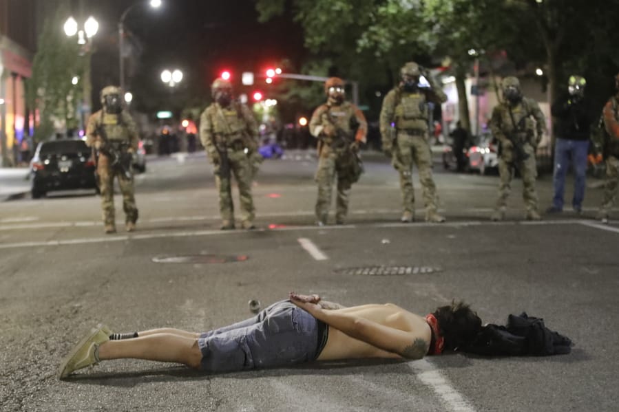 A demonstrator lies down in front of federal officers during a Black Lives Matter protest at the Mark O. Hatfield U.S. Courthouse early Sunday, July 26, 2020, in Portland, Ore. On the streets of Portland, a strange armed conflict unfolds night after night. It is raw, frightening and painful on both sides of an iron fence separating the protesters on the outside and federal agents guarding a courthouse inside. This weekend, journalists for The Associated Press spent the weekend both outside, with the protesters, and inside the courthouse, with the federal agents, documenting the fight that has become an unlikely centerpiece of the protest movement gripping America.
