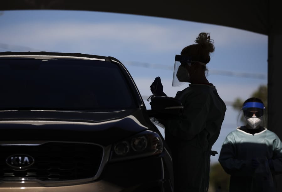 FILE - In this July 10, 2020, file photo healthcare workers test patients in their cars at a drive-thru coronavirus testing site in Las Vegas.
