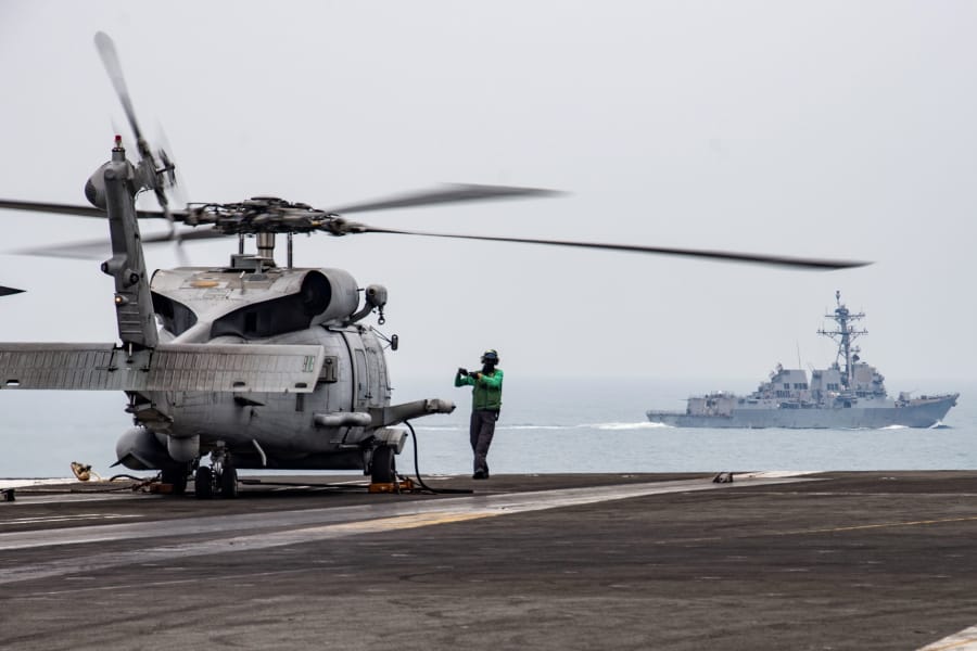 In this photo provided by U.S. Navy, Aviation Electronics Technician 3rd Class James Benzel, from Louisville, Ohio, assigned to the Saberhawks of Helicopter Maritime Strike Squadron, signals an MH-60R Sea Hawk to disengage its rotors on the flight deck of the USS Ronald Reagan (CVN 76) as USS Mustin (DDG 89) steams alongside in South China Sea, Thursday, July 9, 2020. China on Tuesday, July 14, described a U.S. rejection of its maritime claims in the South China Sea as completely unjustified and accused the U.S. of attempting to sow discord between China and the Southeast Asian countries with which it has territorial disputes.