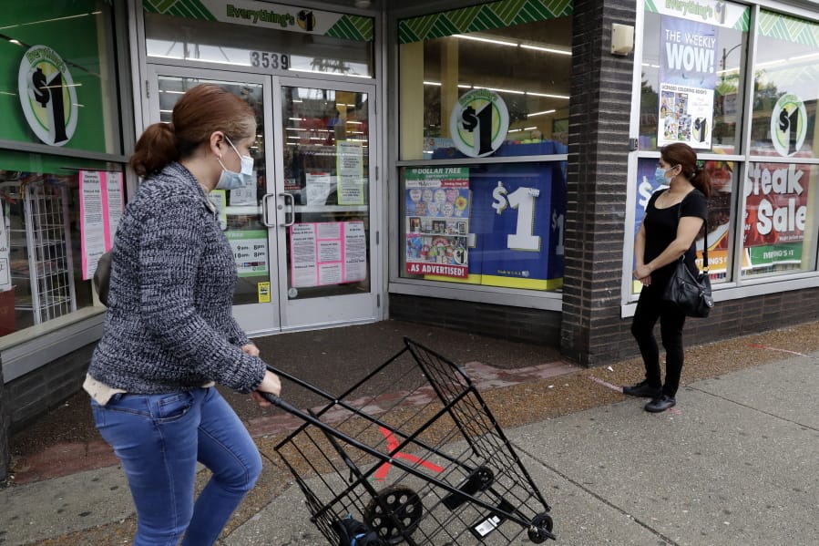 FILE - In this Friday, May 15, 2020, file photo, a woman wearing a mask, left, walks by a Dollar Tree, while another woman waits in line to shop at the store, which is limiting customers amid the coronavirus pandemic, in Chicago. (AP Photo/Nam Y.