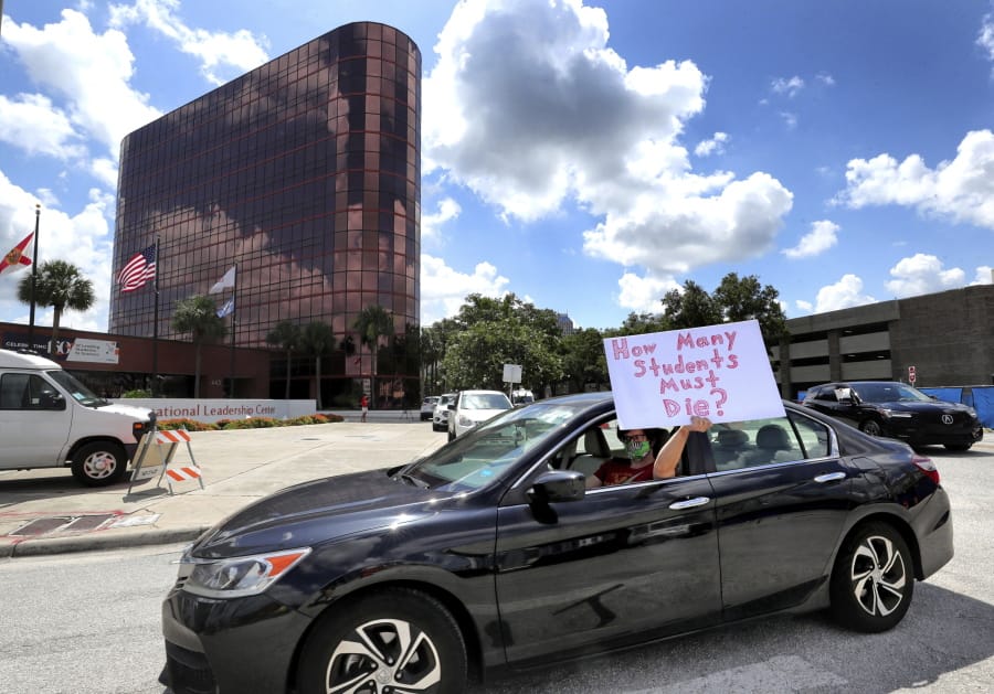 FILE - In this Tuesday, July 7, 2020 file photo, a teacher holds up a sign while driving by the Orange County Public Schools headquarters as educators protest in a car parade around the administration center in downtown Orlando, Fla. As pressure mounts for teachers to return to their classrooms this fall, concerns about the pandemic are pushing many toward alternatives, including career changes, as some mobilize to delay school reopenings in areas hardest hit by the coronavirus. Teachers unions have begun pushing back on what they see as unnecessarily aggressive timetables for reopening.