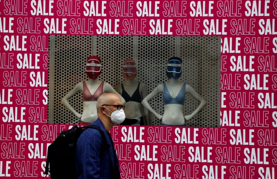 A man wearing a protective face mask walks past a shop window in London, Tuesday, July 14, 2020. Britain&#039;s government is demanding people wear face coverings in shops as it has sought to clarify its message after weeks of prevarication amid the COVID-19 pandemic.