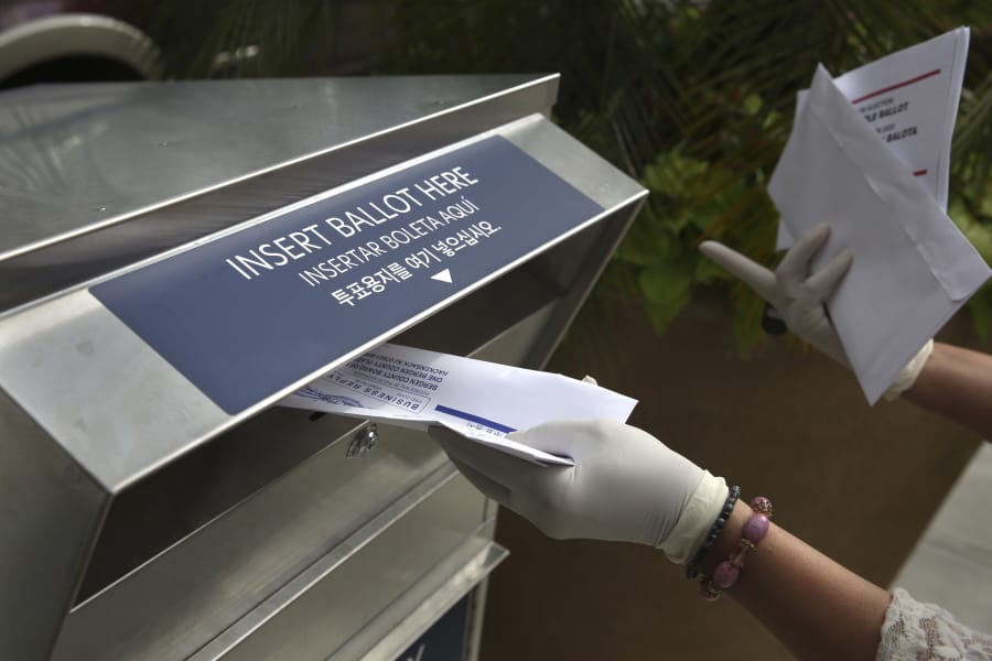 FILE - In this July 7, 2020, file photo a woman wearing gloves drops off a mail-in ballot at a drop box in Hackensack, N.J. The November election is coming with a big price tag as America faces the coronavirus pandemic. The demand for mail-in ballots is surging, election workers are in need of training and polling booths might have to be outfitted with protective shields.