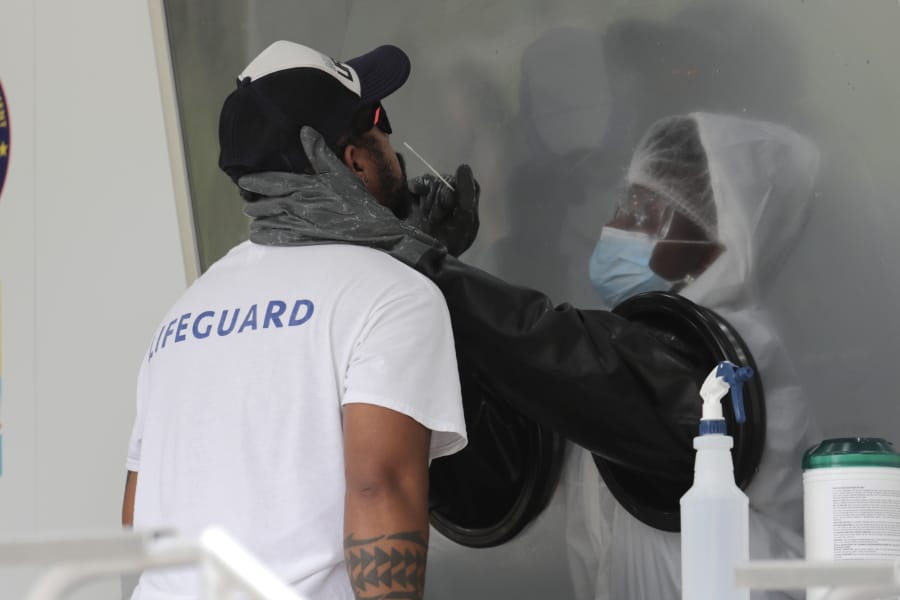 Rafael Ruiz, left, is tested for COVID-19 at a walk-up testing site during the coronavirus pandemic, Friday, July 17, 2020, in Miami Beach, Fla. The mobile testing truck is operated by Aardvark Mobile Health, which has partnered with the Florida Division of Emergency Management. People getting tested are separated from nurses via a glass pane.