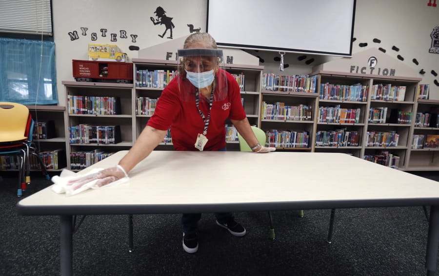 Wearing a mask and face guard as protection against the spread of COVID-19, Garland Independent School District custodian Camelia Tobon wipes down a table in the library at Stephens Elementary School in Rowlett, Texas, Wednesday, July 22, 2020.(AP Photo/LM Otero)
